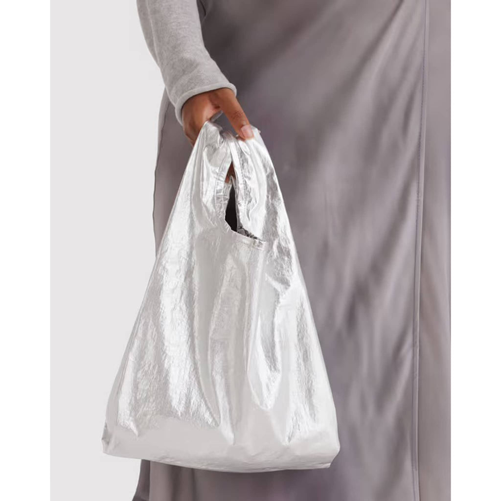 Person holding a silver metallic nylon bag against a plain background.