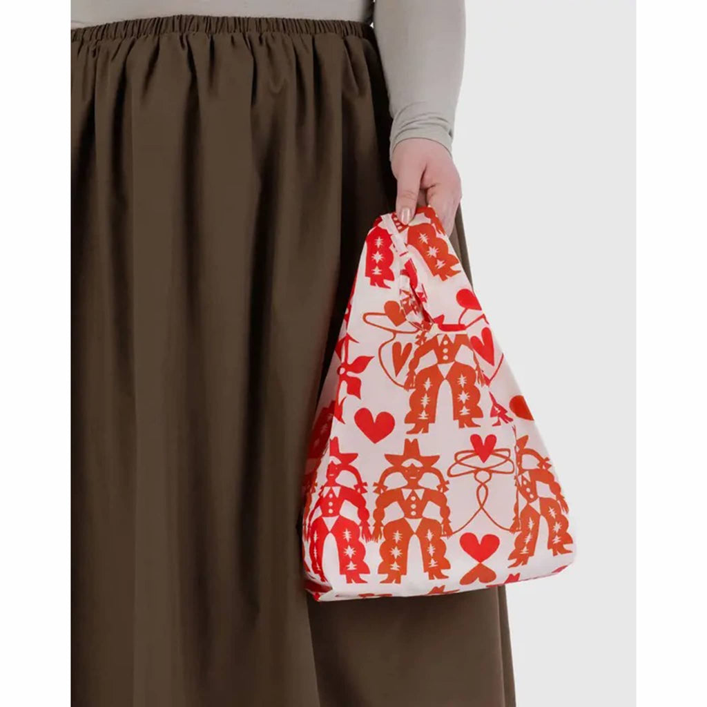 Person holding a red and white patterned bag with brown pants on a white background.