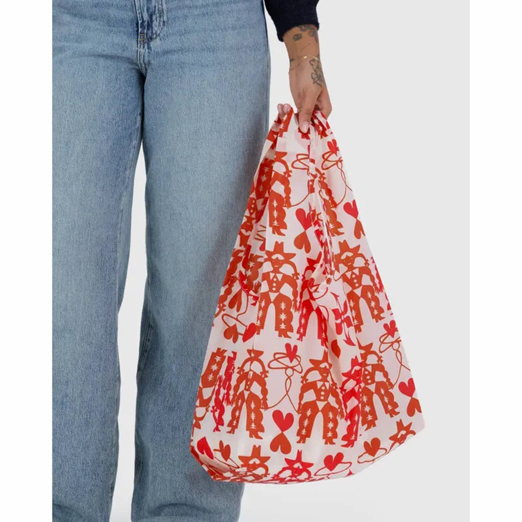Person holding a red and white patterned bag with blue jeans on a white background.