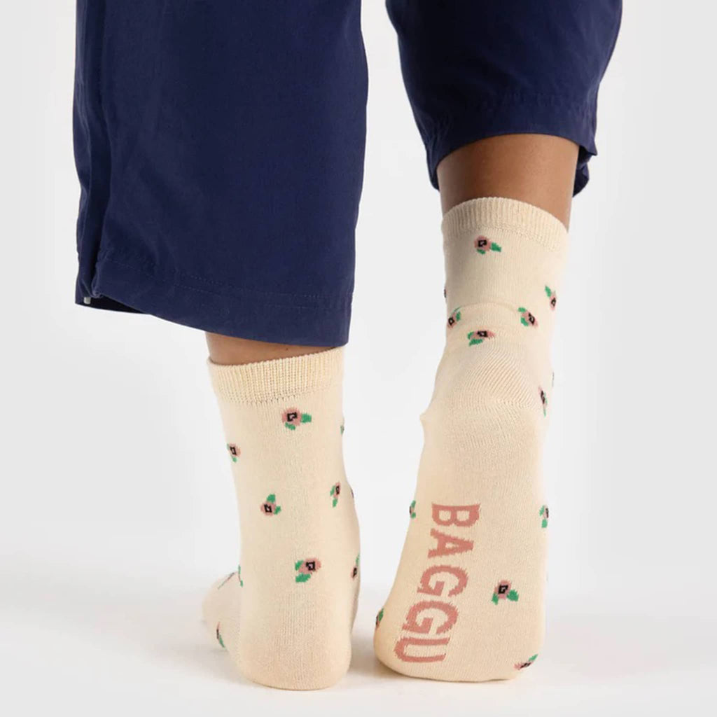 Baggu bamboo rayon unisex Rosette crew socks with small peach flowers on a cream background, being worn by a model, back and sole view.