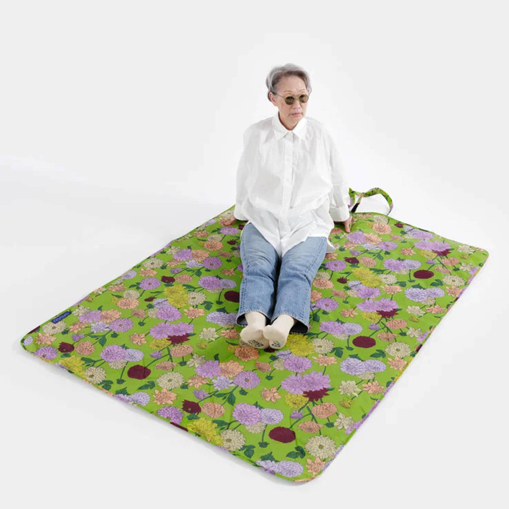 Baggu dahlia puffy recycled ripstop nylon and polyester picnic blanket, flat with a model sitting on it.