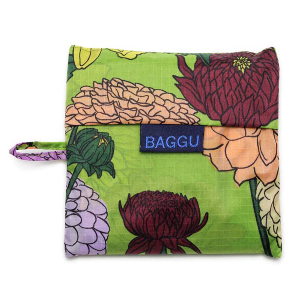 Baggu standard size eco-friendly recycled ripstop nylon reusable tote bag with a colorful dahlia print on a green backdrop, in matching pouch.