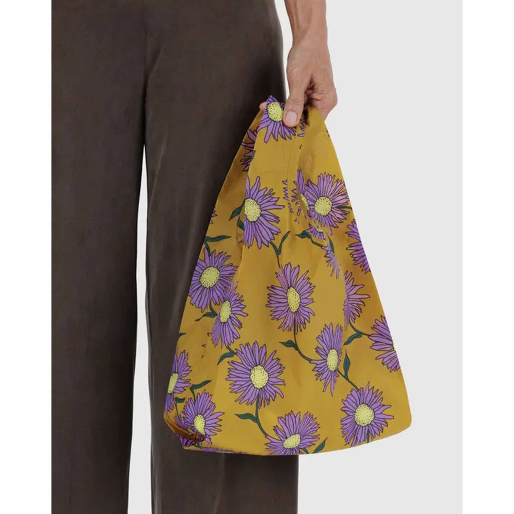 Person holding a mustard yellow bag with purple floral pattern.