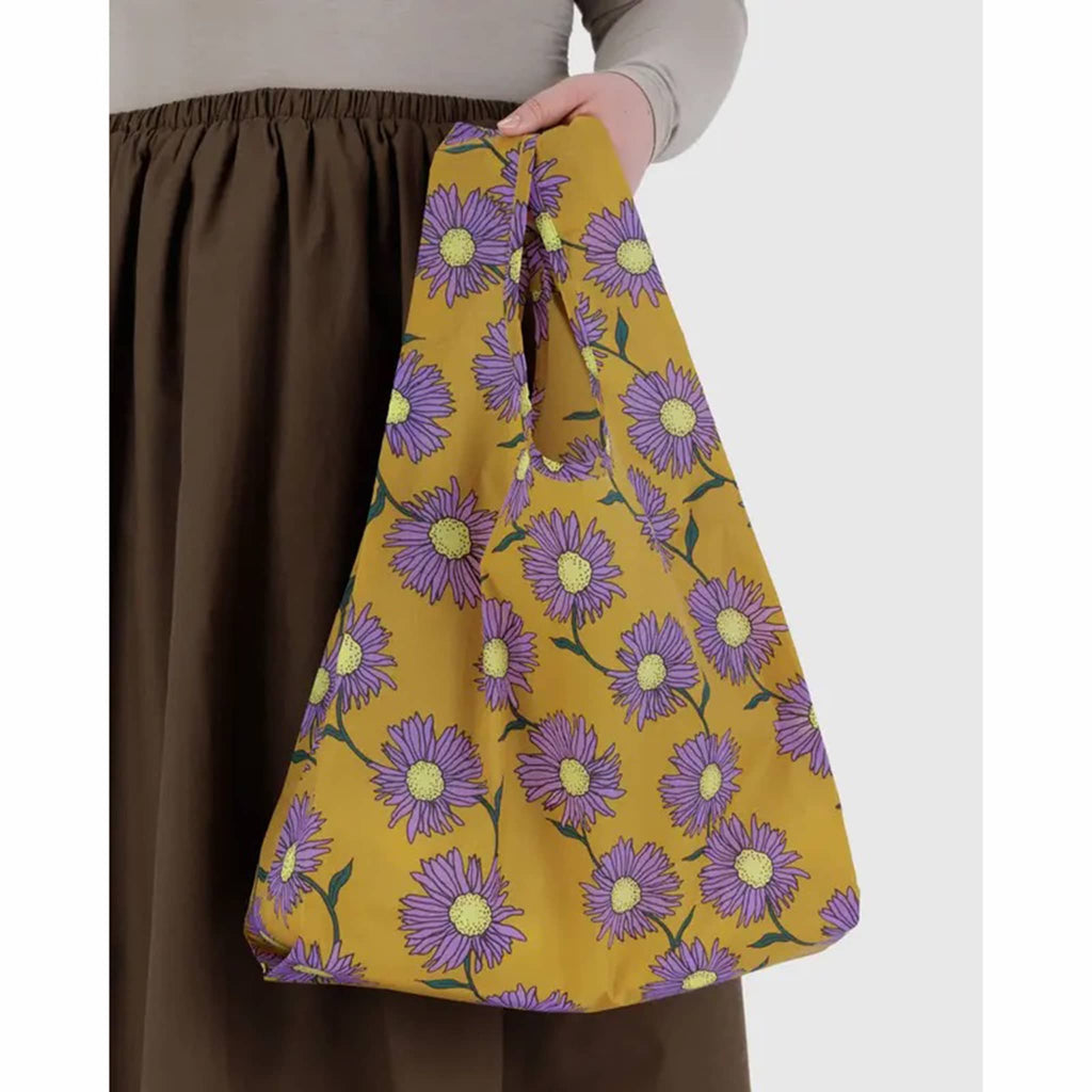 Person holding a yellow bag with purple floral pattern on a white background