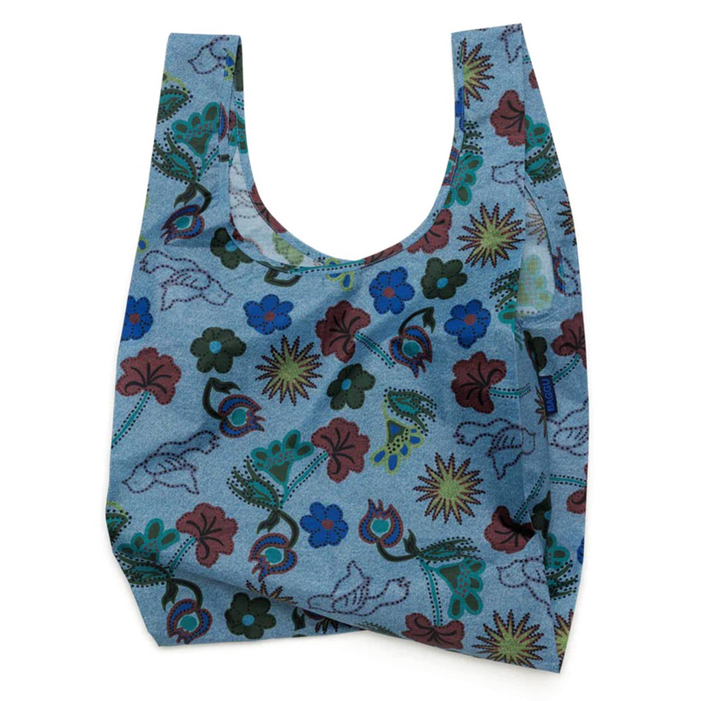Baggu standard size eco-friendly recycled ripstop nylon reusable tote bag with floral and bird illustrations on denim colored backdrop, unfolded.