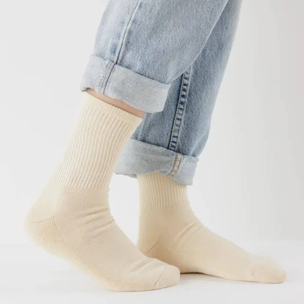 Ribbed ecru socks worn with rolled-up blue jeans on a light gray background.