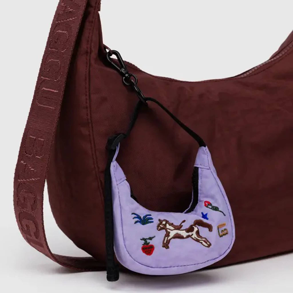 Baggu purple crescent bag charm with embroidered horse design and black strap clipped on a larger mahogany colored crescent bag.
