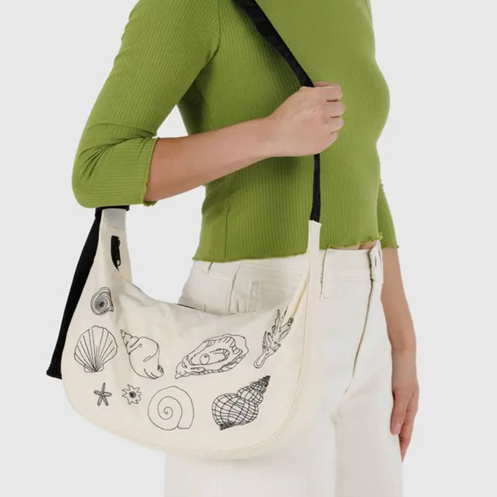 Baggu embroidere shells medium ripstop nylon crescent bag, on model's shoulder.