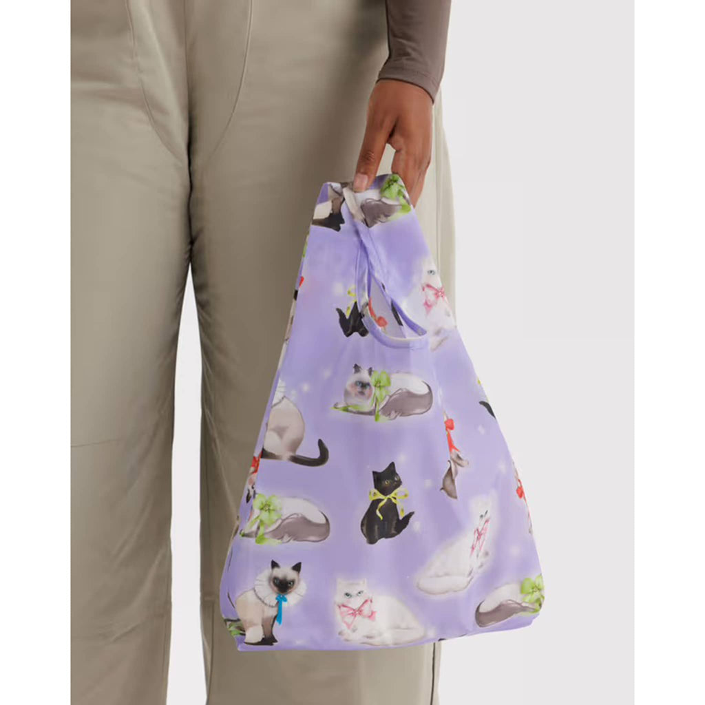 Person holding a purple reusable bag with cat pattern.