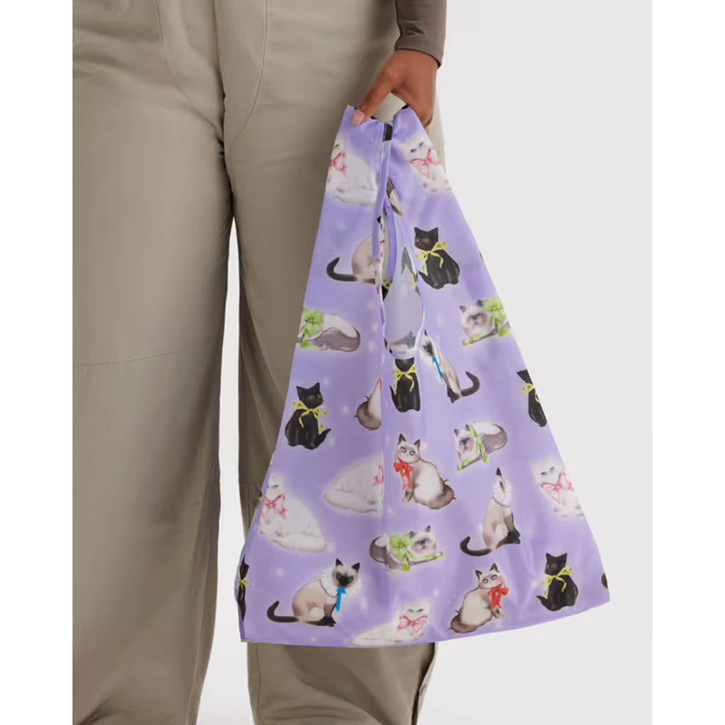 Person holding a purple reusable bag with cat pattern against a gray background.