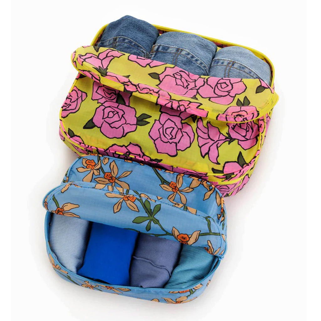 Baggu reusable recycled ripstop nylon packing cube set of 2, large is in rose print and the small cube has the orchid print, partially unzipped and filled with clothing.
