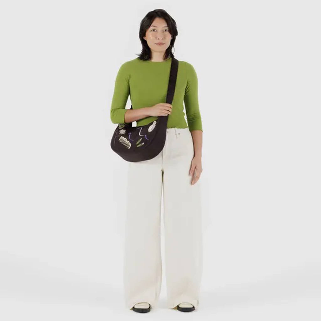 Baggu Medium Crescent Bag in Get Ready With Me embroidered on a black backdrop, with crossbody strap on model.