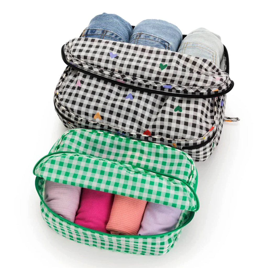 Baggu reusable recycled ripstop nylon packing cube set of 2, large is black and white gingham with colorful hearts and the small cube is green and white gingham print, unzipped and filled with clothing.