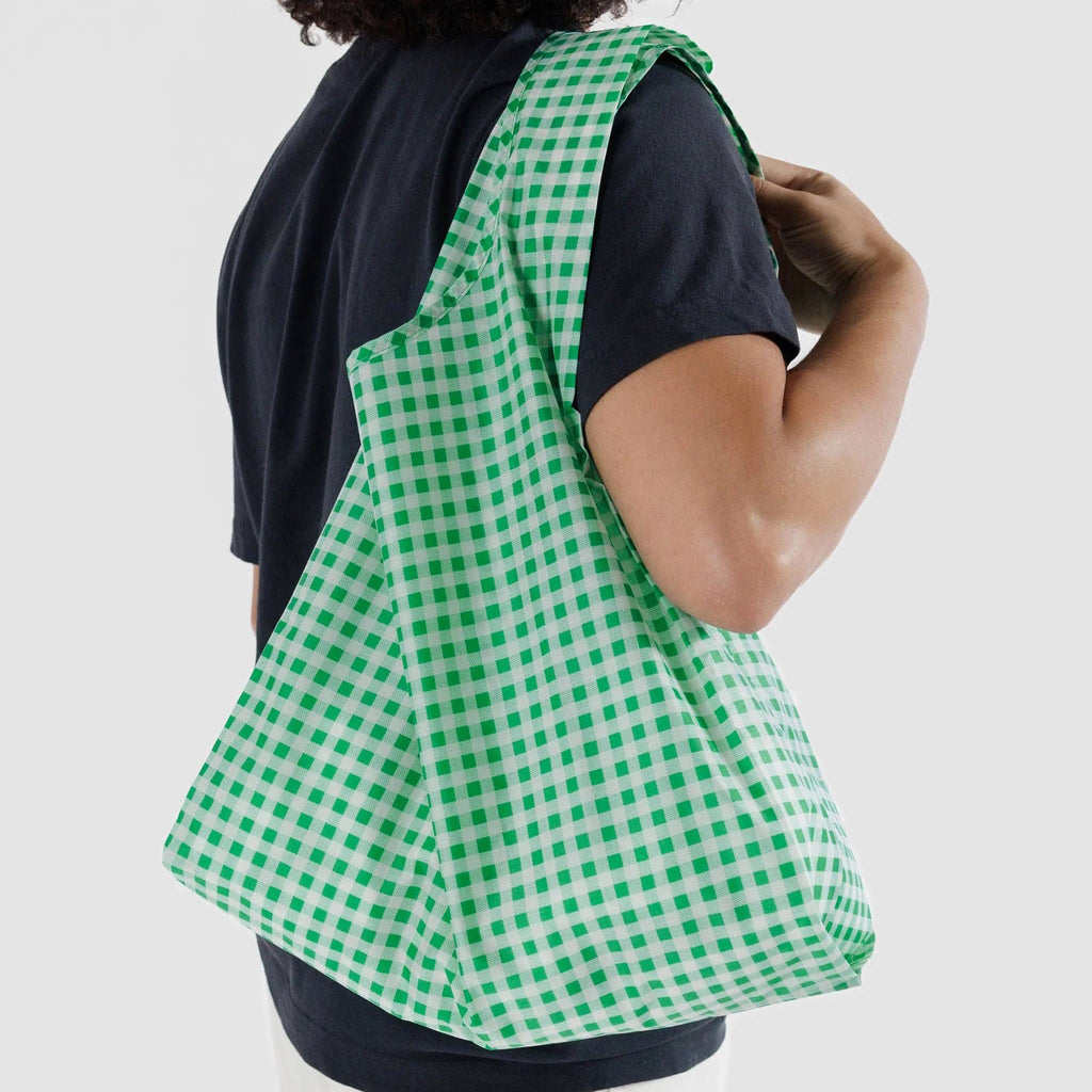 Baggu standard size eco-friendly recycled ripstop nylon reusable tote bag with green and white gingham, on a model's shoulder.