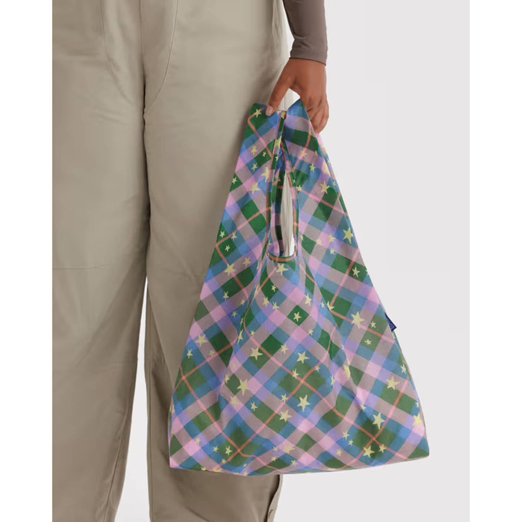 Person holding a colorful plaid bag against a white background.