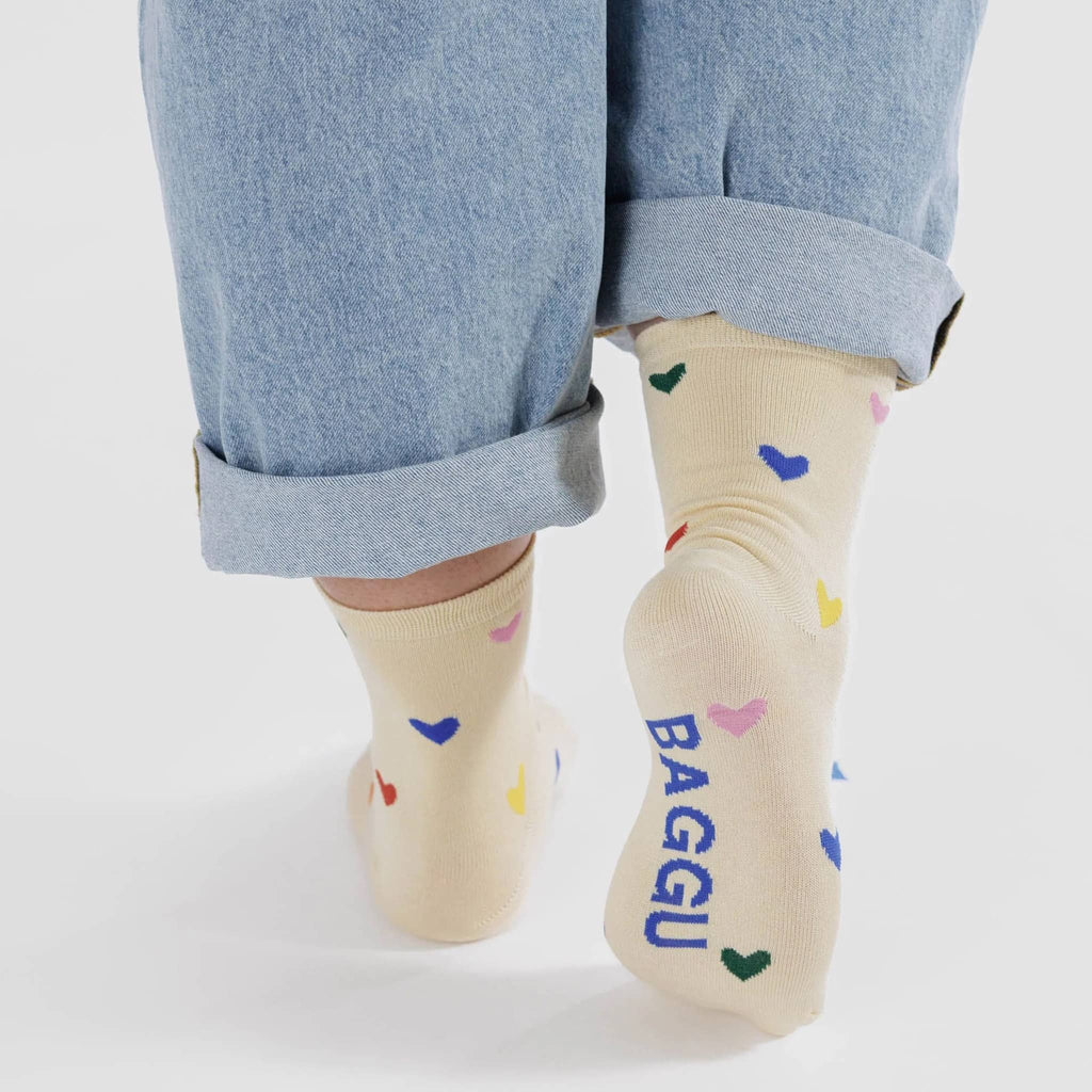 Baggu bamboo rayon unisex crew socks with with colorful hearts on an ecru backdrop, being worn by a model.