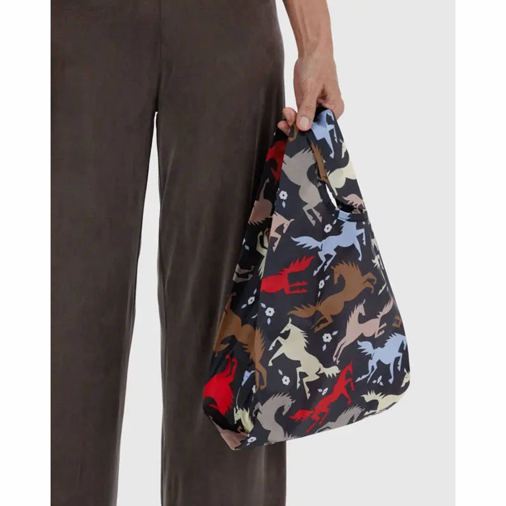 Person holding a patterned bag with horse designs on a plain background.