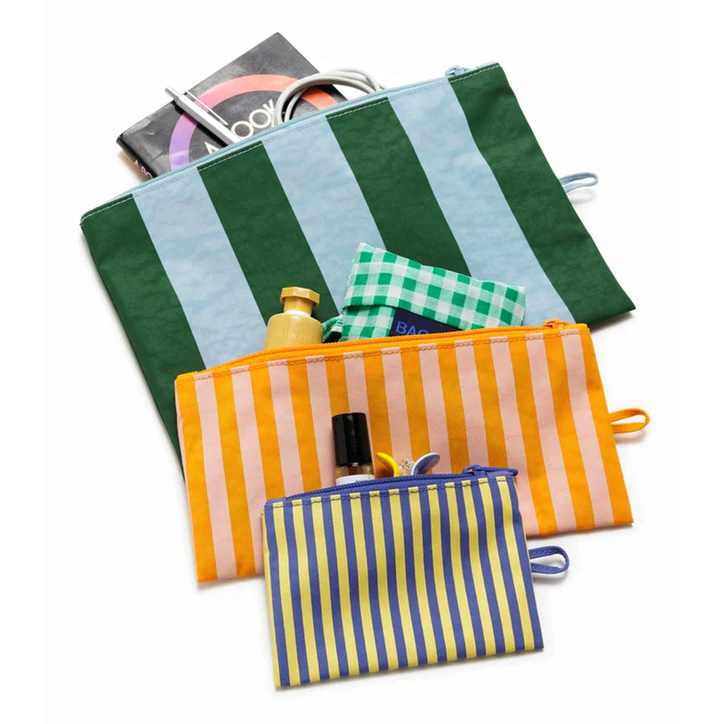 Baggu recycled ripstop nylon flat zipper pouches, set of 3 in assorted sizes with prints from the Hotel Stripes collection, flat and unzipped with hand cream, a book, power cord and hair clip coming out of the tops.