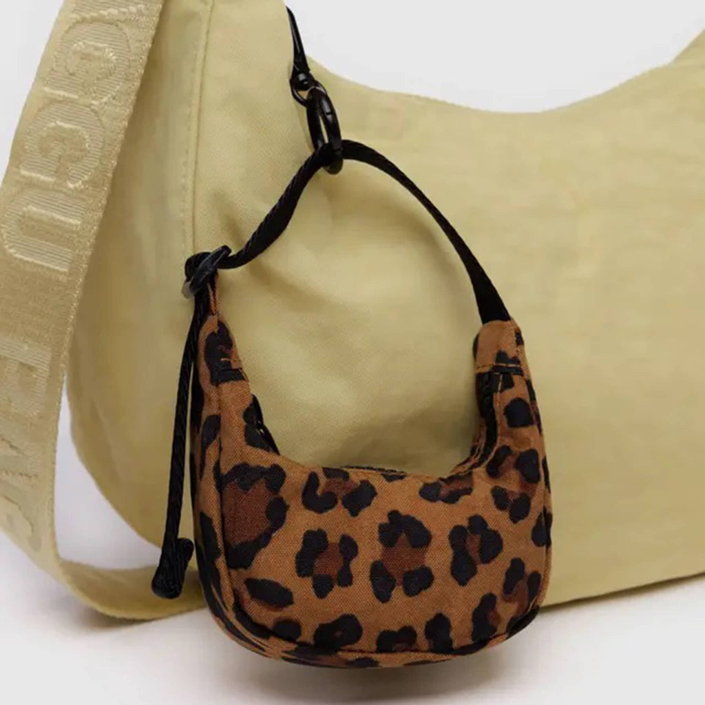 Baggu leopard print crescent bag charm with black strap clipped on a larger Baggu crescent bag in mustard yellow.