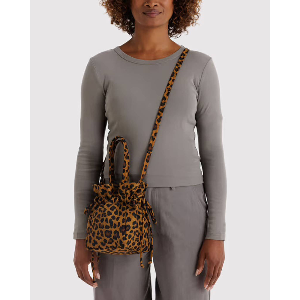 Woman wearing a crossbody leopard print drawstring bag with gray long-sleeve top and pants on a white background.