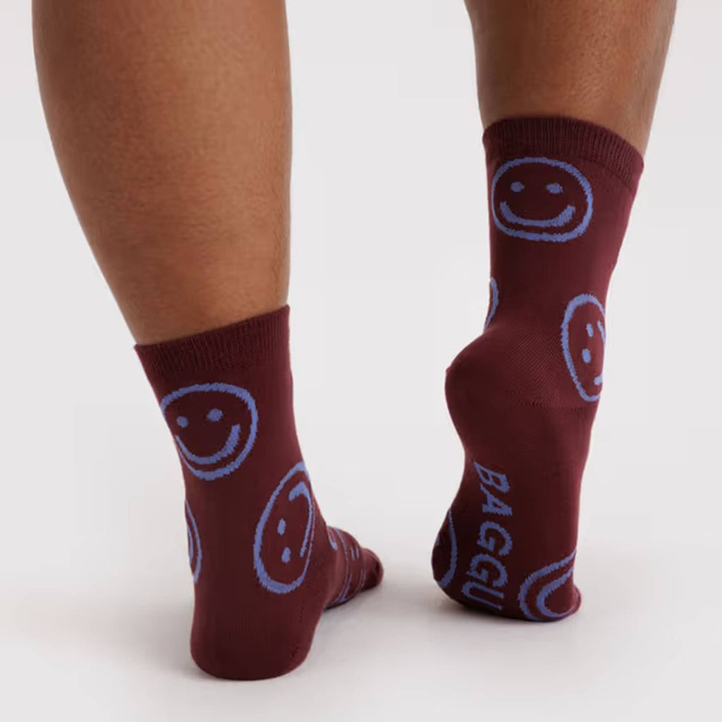 Maroon socks with blue smiley face patterns worn by a person on a white background.