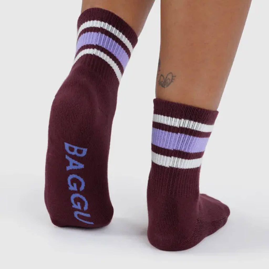 Maroon socks with purple and white stripes worn by a person on a light gray background.
