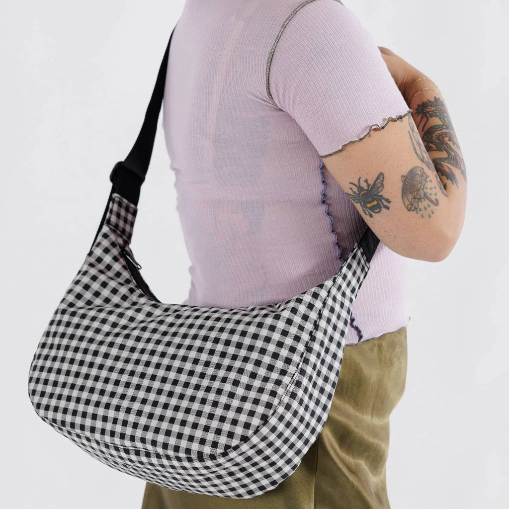 Baggu Medium Ripstop Nylon Crescent Bag in black and white gingham pattern, on model's shoulder.