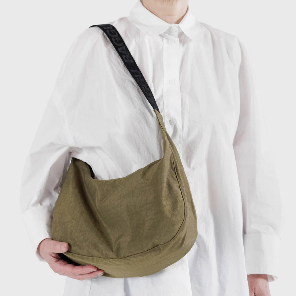 Baggu Medium Ripstop Nylon Crescent Bag in Seaweed, a khaki brown green color, on model's shoulder.