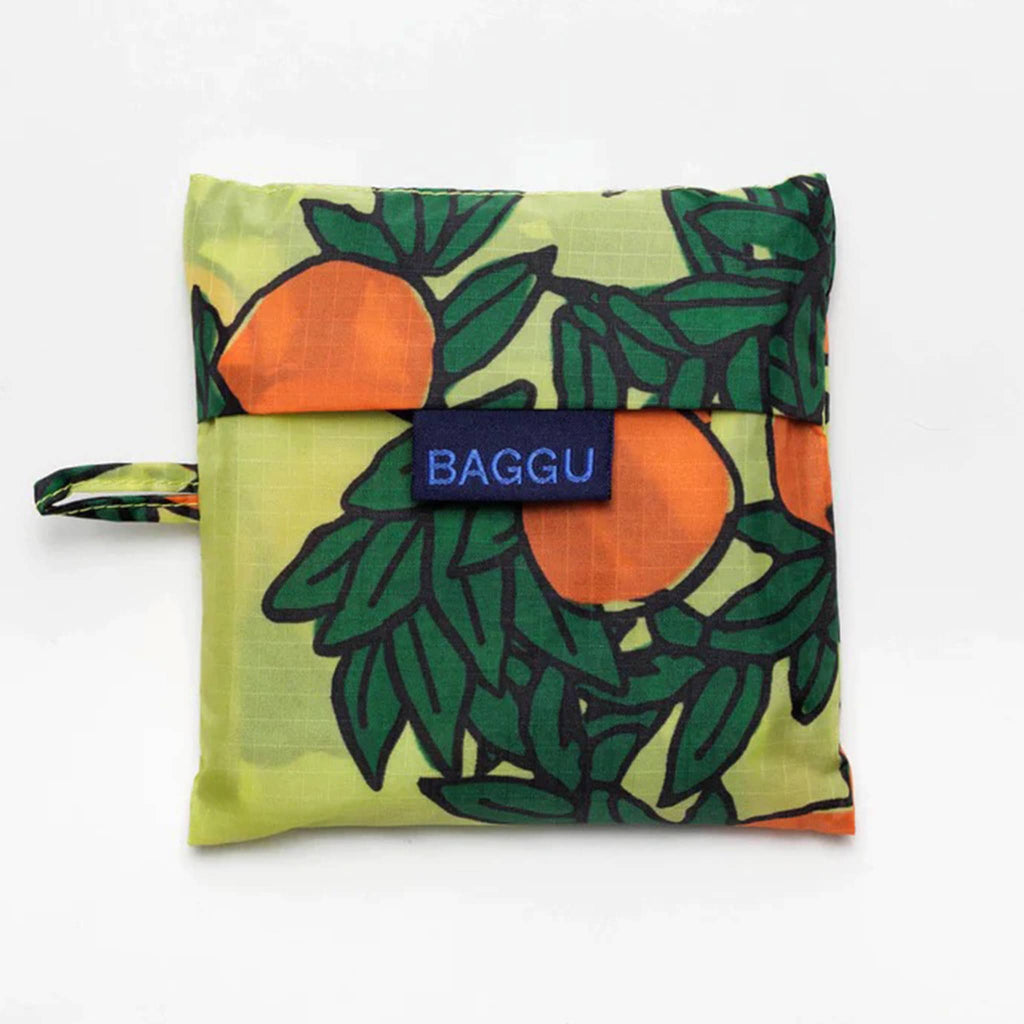 Baggu standard size eco-friendly recycled ripstop nylon reusable tote bag with an orange tree print on a yellow backdrop, in matching pouch.