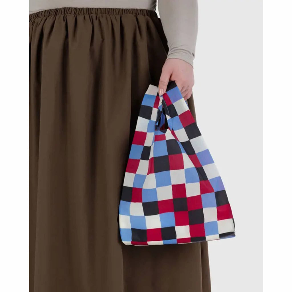 Person holding a multicolored checkered bag against a plain background.