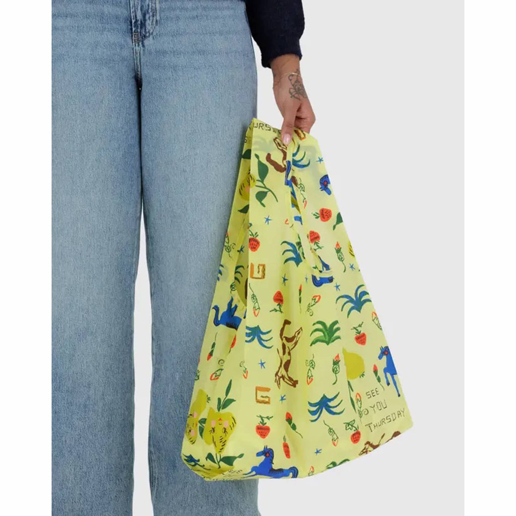 Person holding a yellow reusable bag with colorful animal and nature graphics.