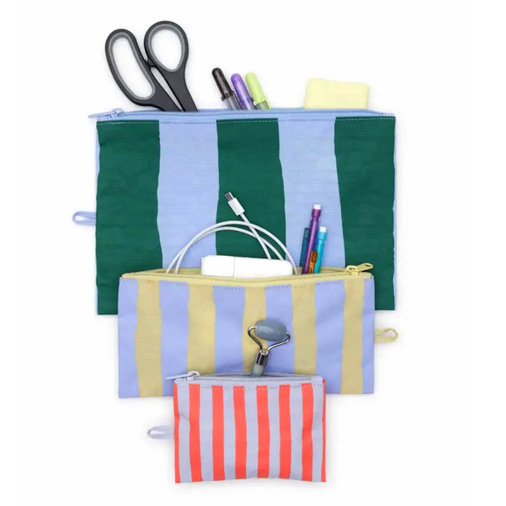 Baggu Painted Stripe recycled heavyweight nylon flat zipper pouch, set of 3 in different colored stripes, with office supplies, chargers and beauty products spilling out the top.