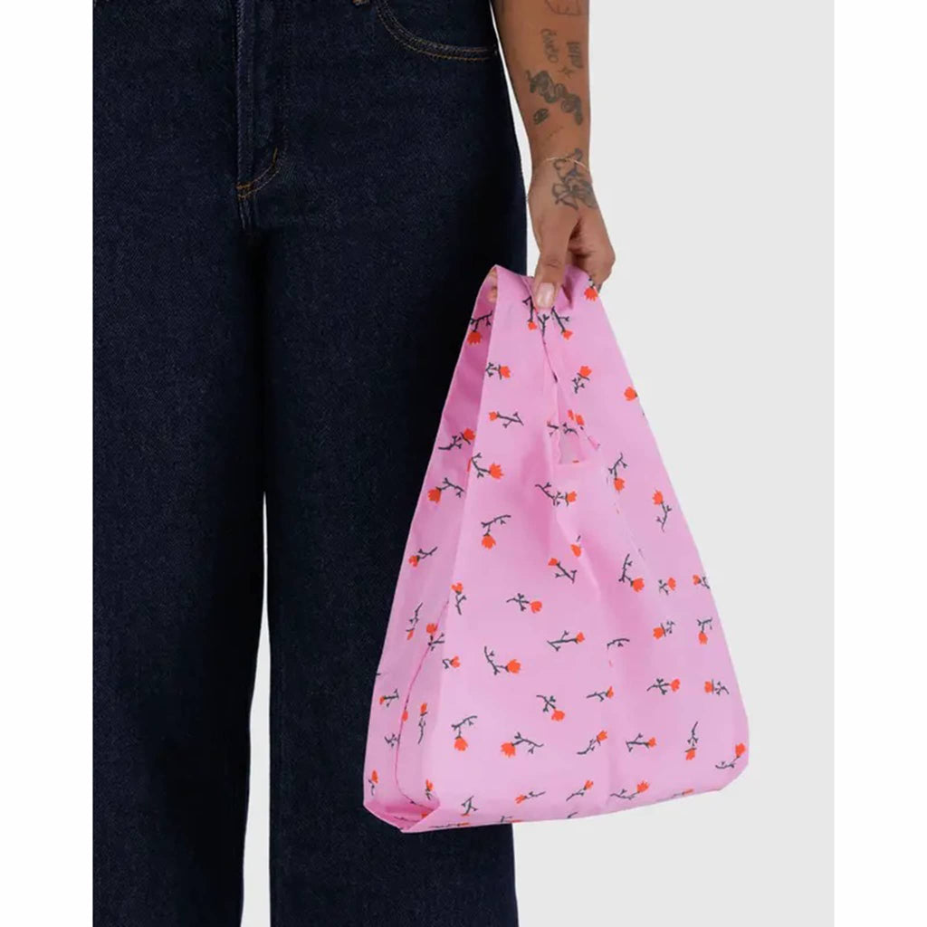 Person holding a pink reusable bag with floral pattern on a white background.