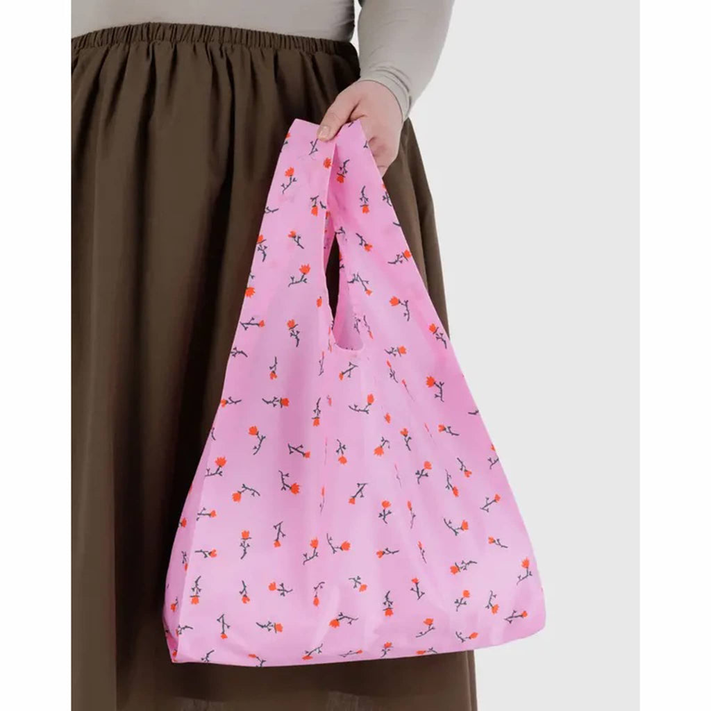 Person holding a pink reusable bag with floral pattern on a white background