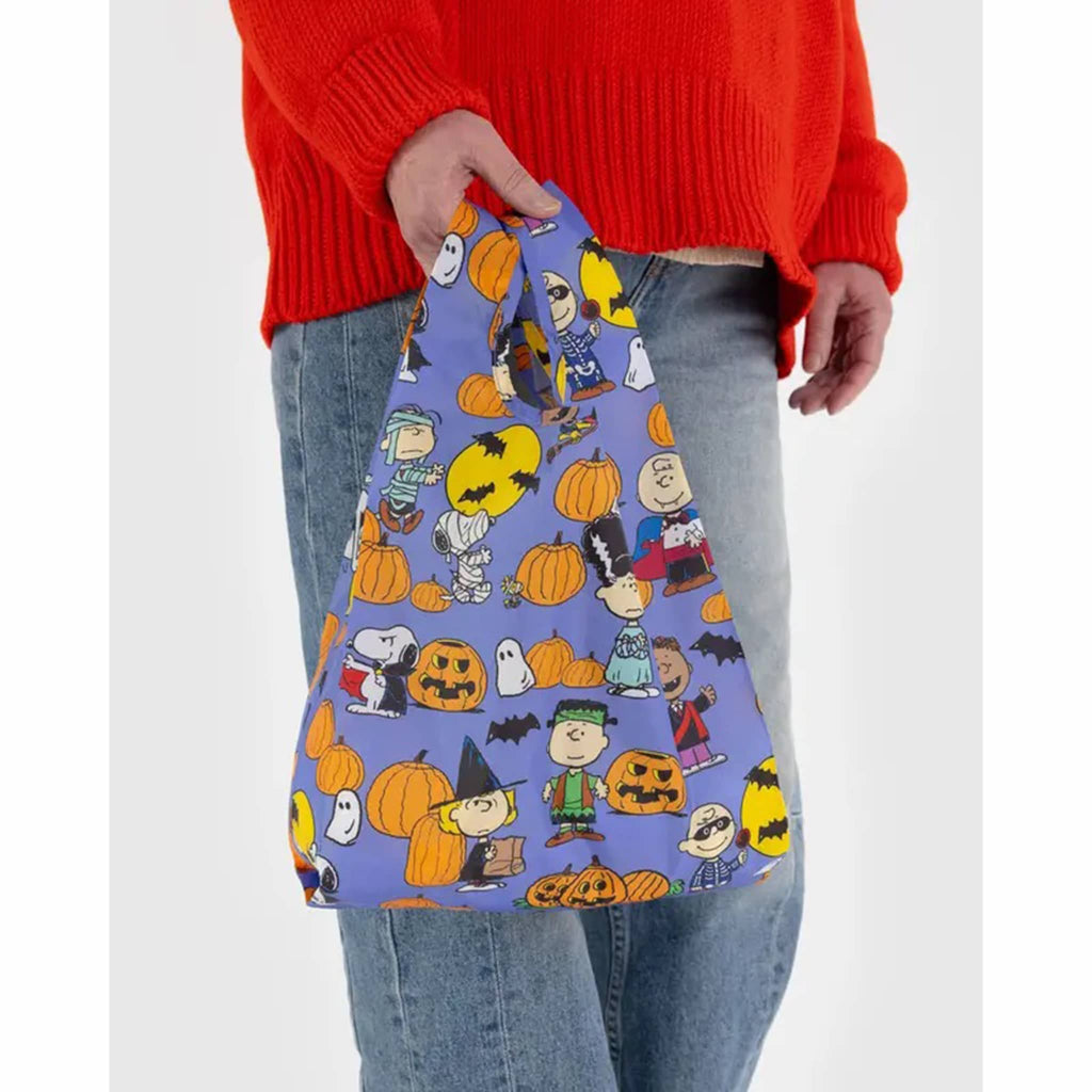 Baby Baggu reusable shopping bag with the Peanuts Pumpkin Patch print on a blue backdrop, in a person's hand.