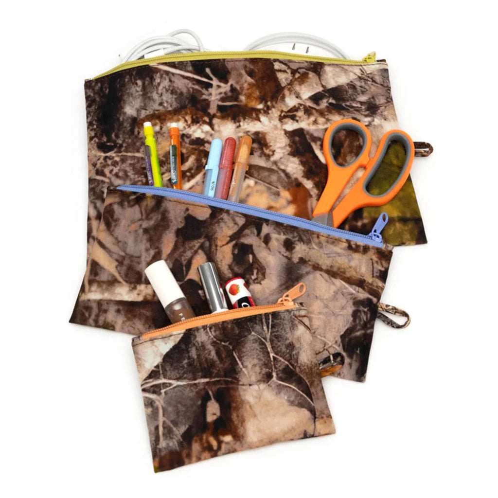 Baggu recycled ripstop nylon flat zipper pouches, set of 3 in assorted sizes with the Photo Forest print, unzipped and filled with cosmetics, art supplies and charging cords.