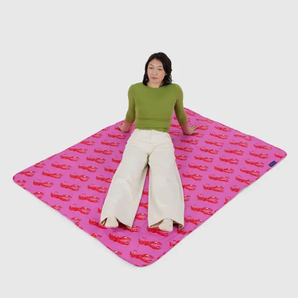 Baggu Pink Lobster puffy recycled ripstop nylon and polyester picnic blanket with a model lying on it.