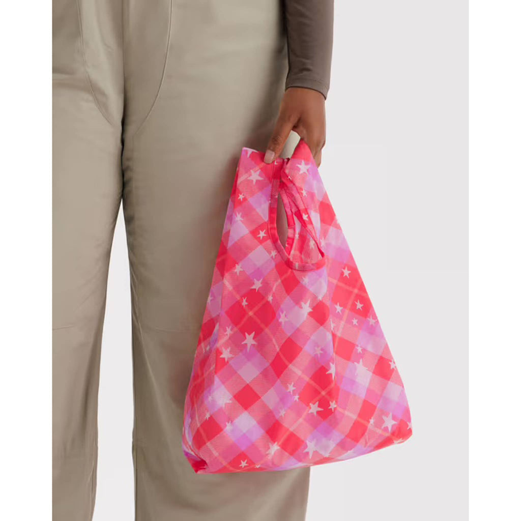 Person holding a pink and white plaid bag with stars on a plain background.