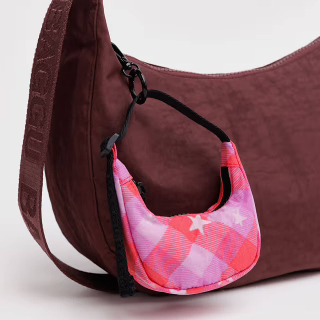 Baggu Pink Star Plaid print crescent bag charm clipped to a larger burgundy crescent bag, on a white background.