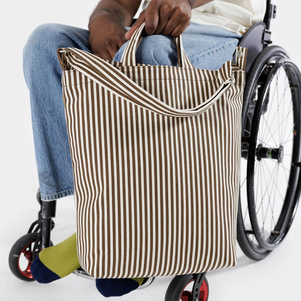 Baggu recycled cotton canvas duck bag tote with zip top closure in brown and cream stripes, in hand of model in a wheelchair.