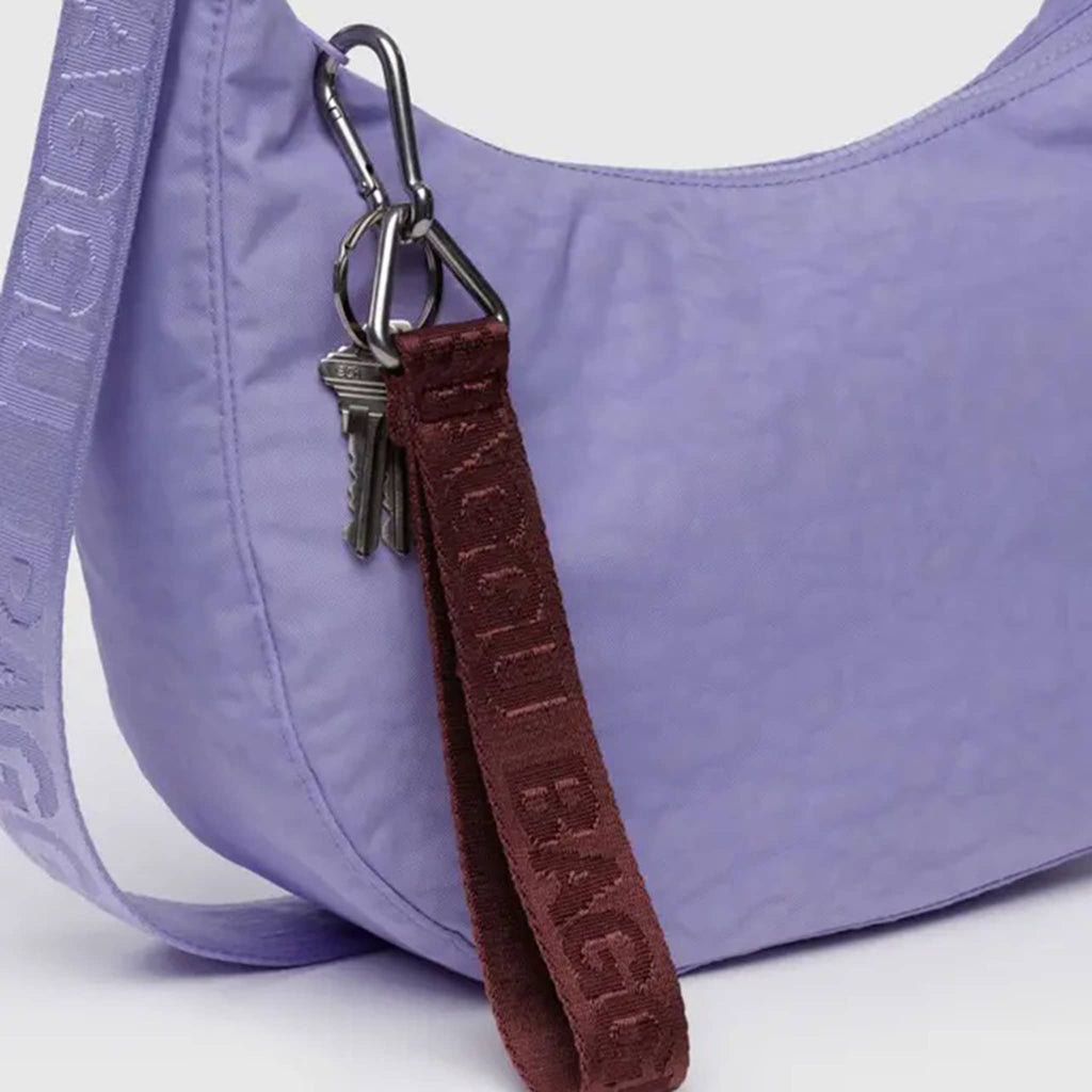 A burgundy webbed nylon keychain with the Baggu logo, featuring a metal clip and a triangle ring, shown clipped to a larger purple Baggu Crescent Bag.