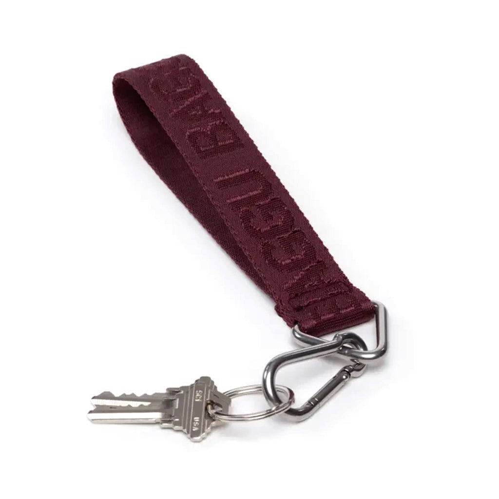 A burgundy webbed nylon keychain with the Baggu logo, featuring a metal clip and a triangle ring, with keys.