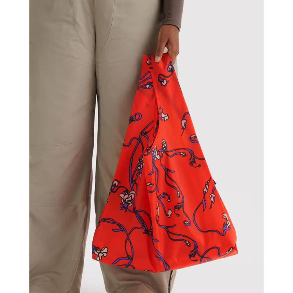 Person holding a red floral patterned bag against a white background.