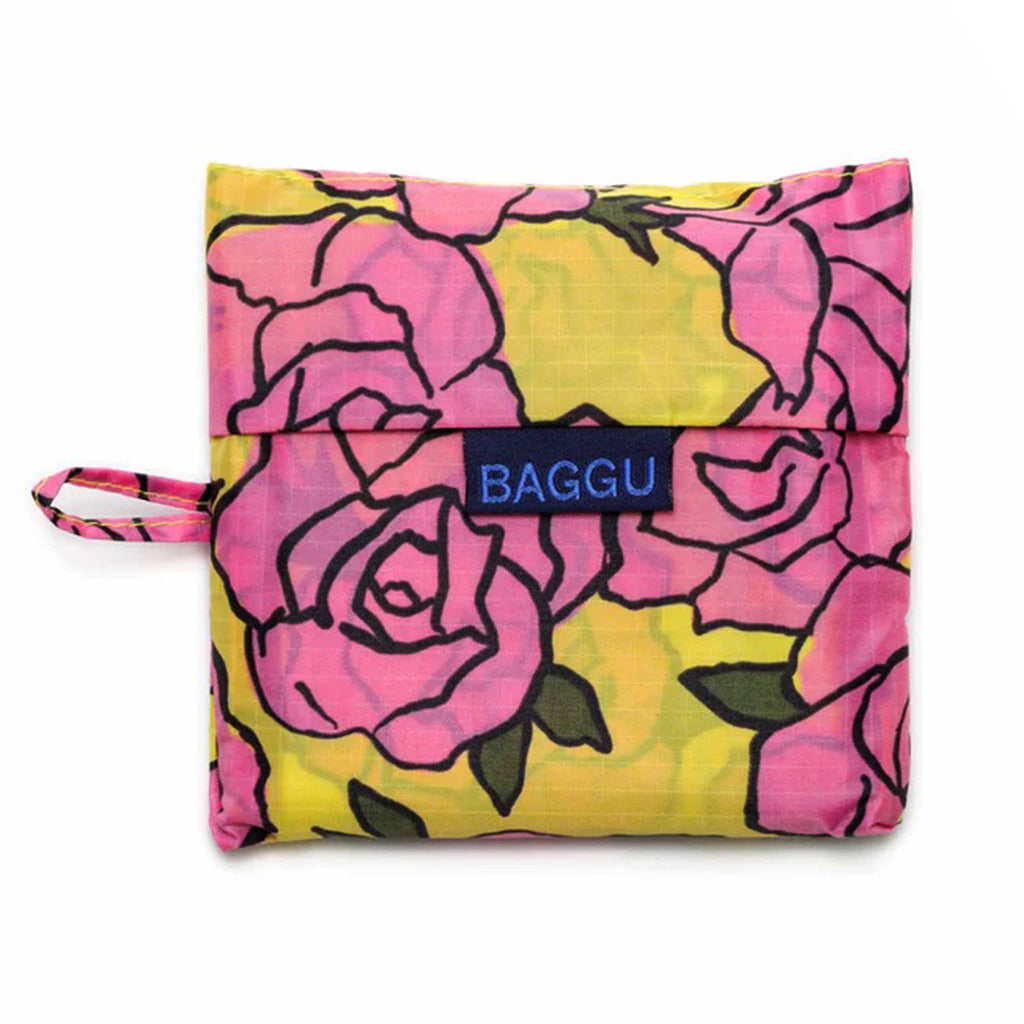 Baggu standard size eco-friendly recycled ripstop nylon reusable tote bag with a pink rose print on a yellow backdrop, in matching pouch.