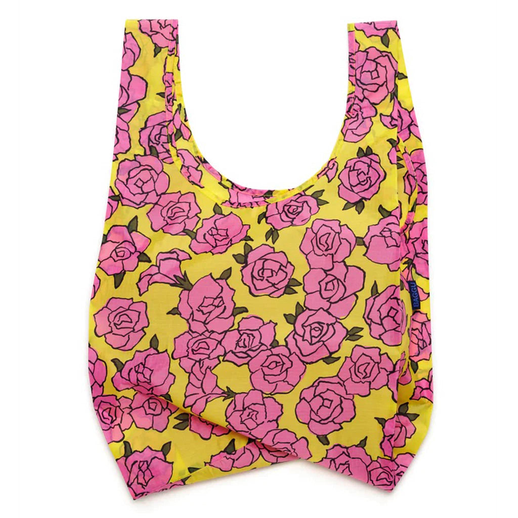 Baggu standard size eco-friendly recycled ripstop nylon reusable tote bag with a pink rose print on a yellow backdrop, unfolded.