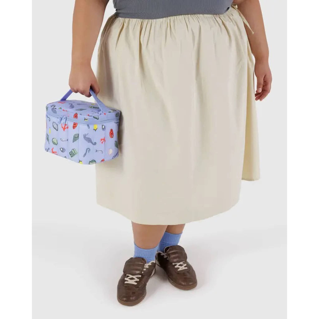 Baggu Insulated Puffy Nylon Lunch Bag with Sea Charms print and a periwinkle zipper and handle, in models hand.