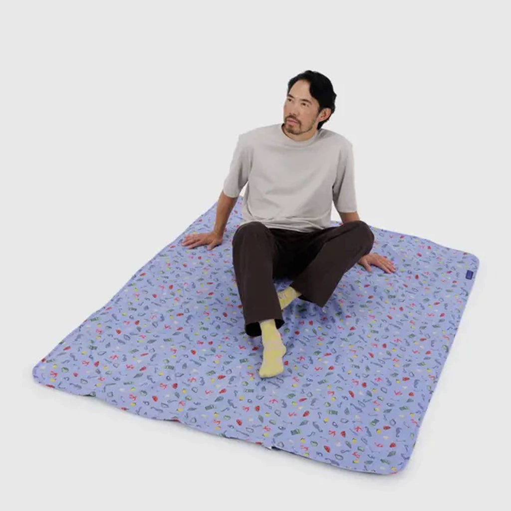 Baggu Sea Charms puffy recycled ripstop nylon and polyester picnic blanket with model on it.