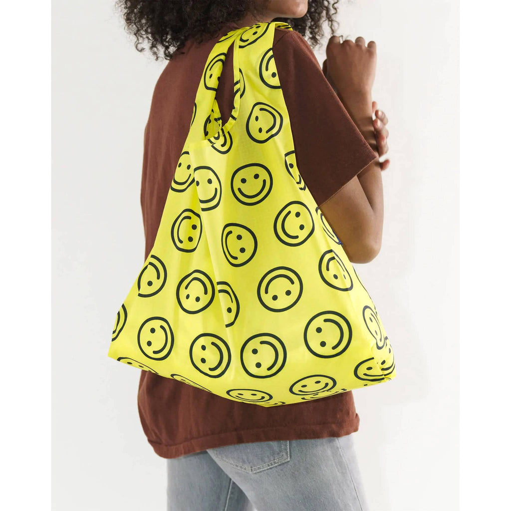 Bright yellow Baggu standard bag with repeating black smiley faces on a model's shoulder.