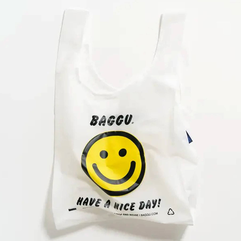 Baggu reusable standard white ripstop nylon bag in thank you happy with yellow smiley face and have a nice day in black text, unfolded.