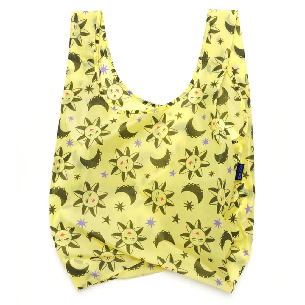 Baggu standard size eco-friendly recycled ripstop nylon reusable tote bag with a sun and moon charms print on a yellow backdrop, unfolded.